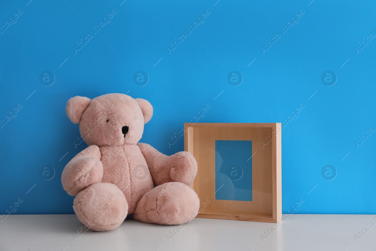 Photo of Empty photo frame and teddy bear on white table near light blue wall. Space for design