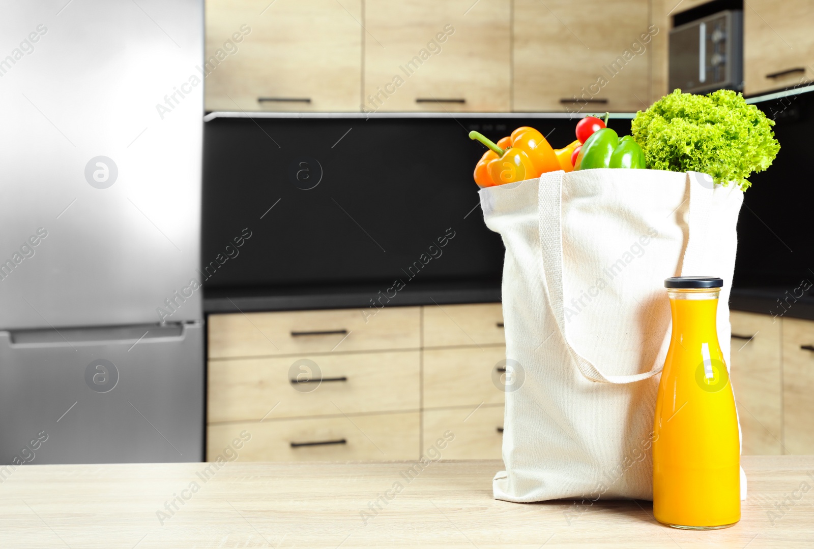 Photo of Tote bag with vegetables and bottle of juice on wooden table in kitchen. Space for text