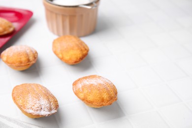 Photo of Delicious madeleine cookies and baking mold on white tiled table, closeup. Space for text