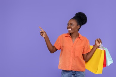 Photo of Happy young woman with shopping bags pointing at something on purple background. Space for text