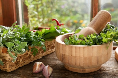 Photo of Mortar with pestle and fresh green herbs on wooden table