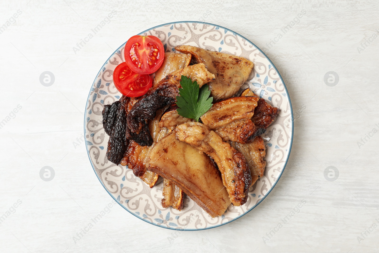 Photo of Tasty fried pork lard with parsley and tomatoes on white wooden table, top view