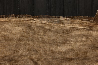 Burlap fabric on black wooden table, top view