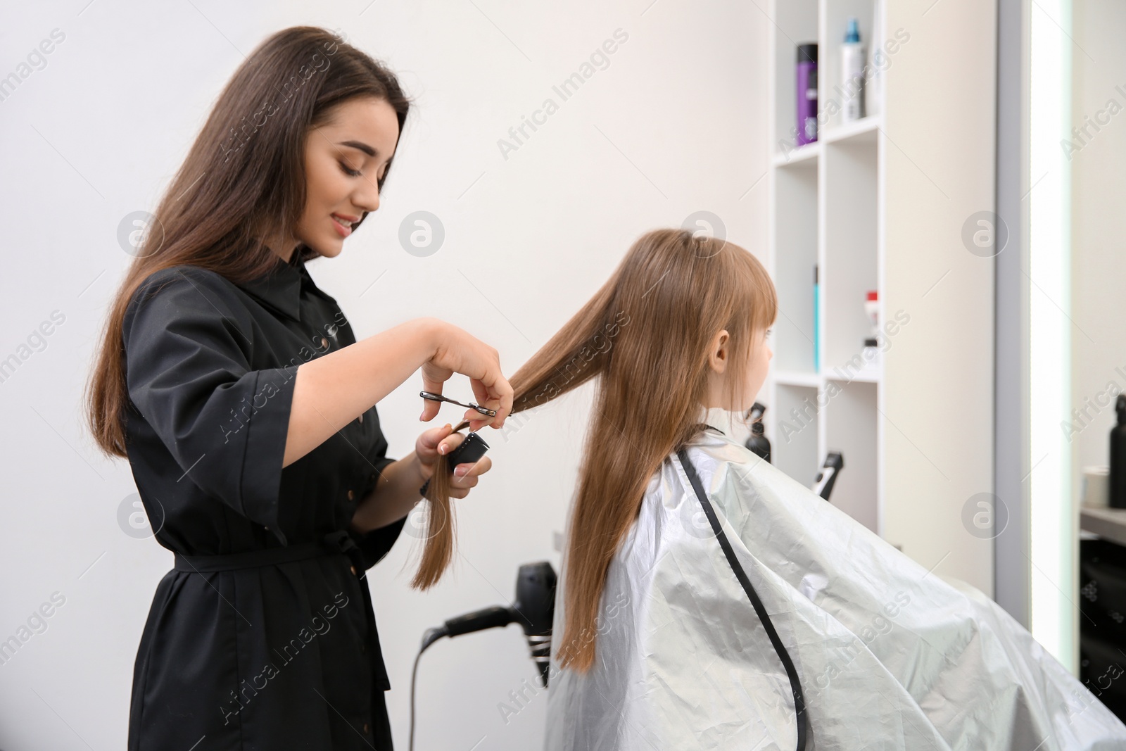 Photo of Professional female hairdresser working with little girl in salon