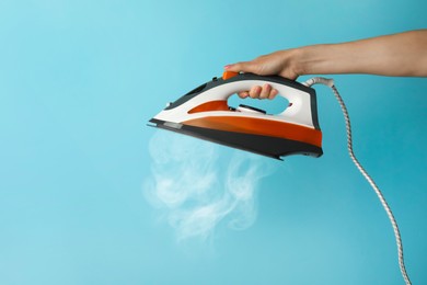 Image of Woman holding modern iron with steam on turquoise background, closeup. Space for text