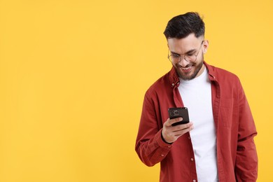 Happy young man using smartphone on yellow background, space for text