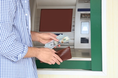 Man with money near cash machine outdoors, closeup