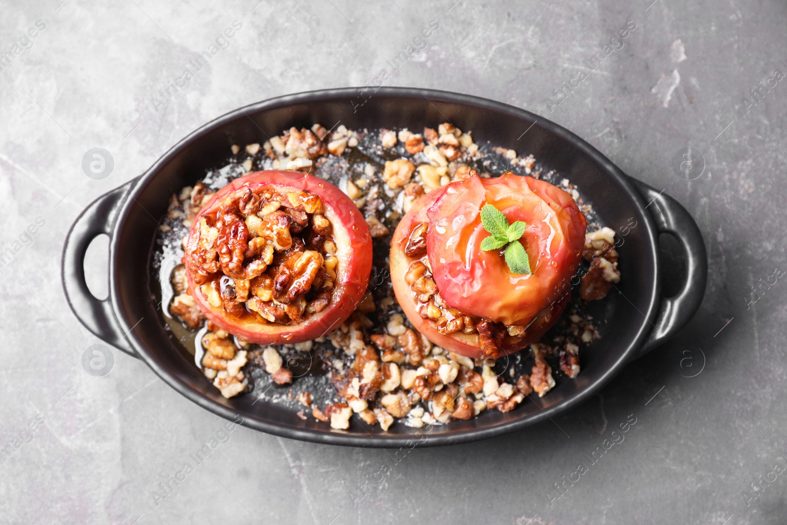 Photo of Tasty baked apples with nuts, honey and mint in baking dish on gray textured table, top view