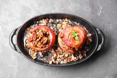 Photo of Tasty baked apples with nuts, honey and mint in baking dish on gray textured table, top view