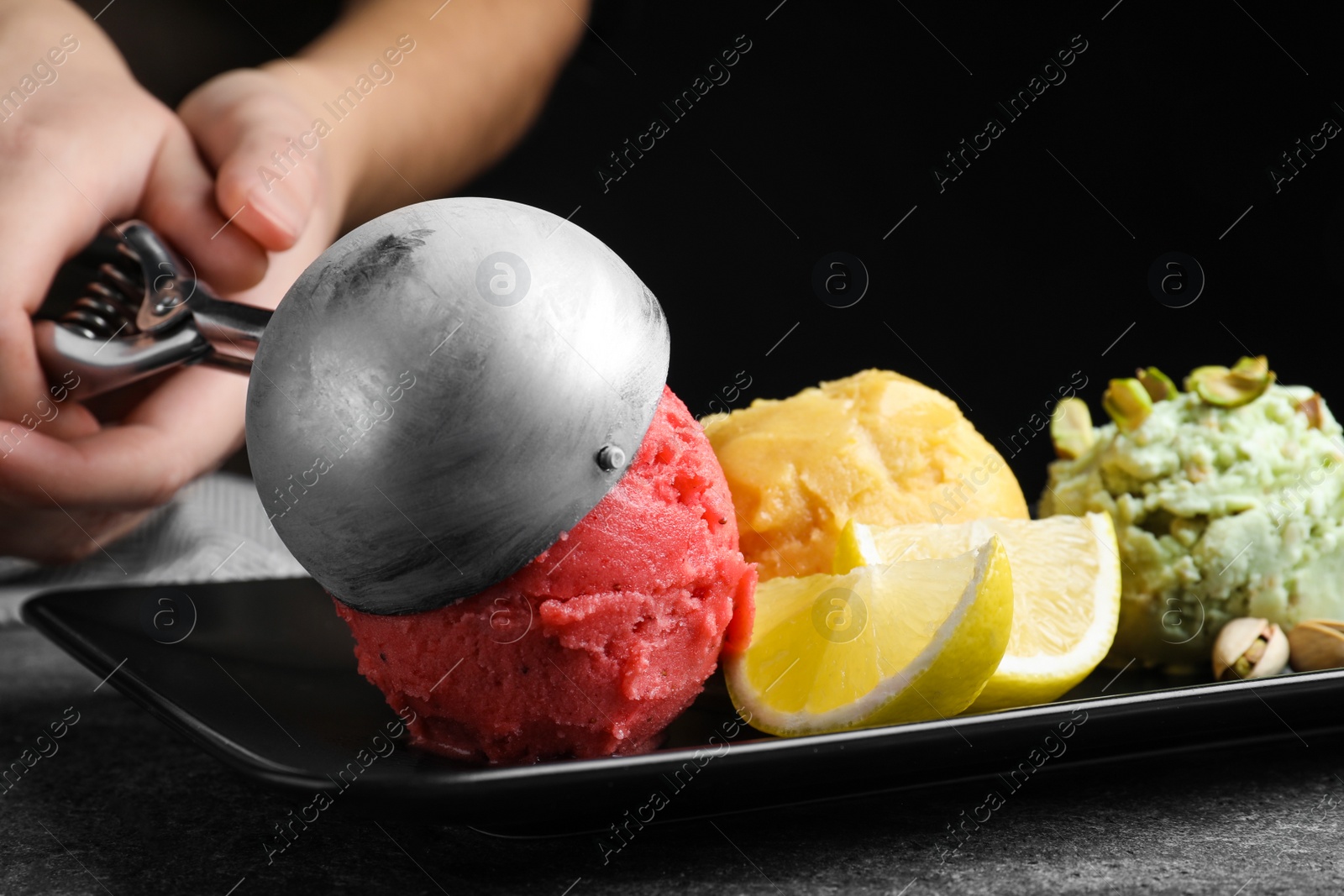 Photo of Woman putting strawberry ice cream scoop onto plate, closeup