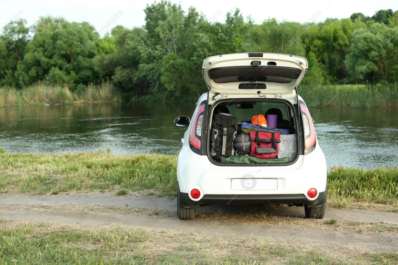 Photo of Car with camping equipment in trunk on riverbank. Space for text