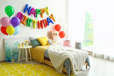 Photo of Phrase HAPPY BIRTHDAY made of colorful balloon letters and table with treats in modern bedroom