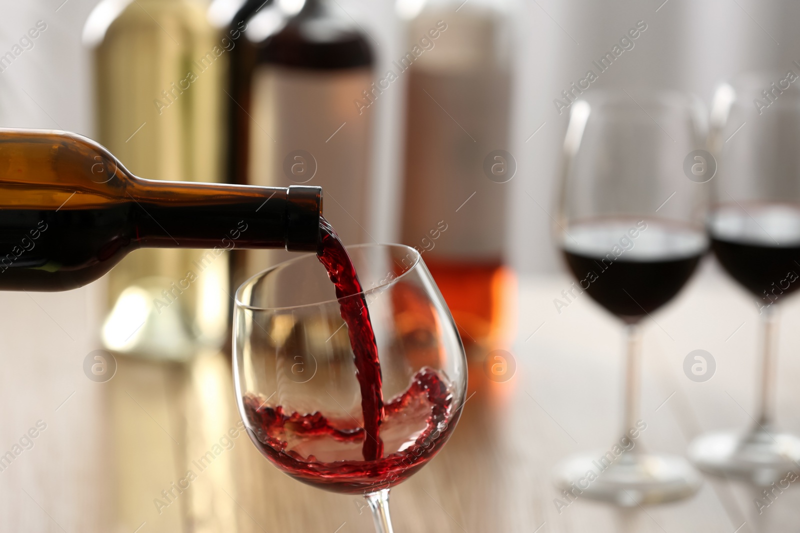 Photo of Pouring red wine from bottle into glass on blurred background, closeup. Space for text