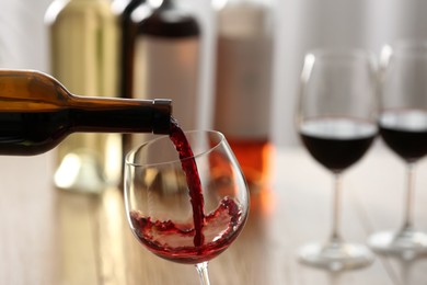 Photo of Pouring red wine from bottle into glass on blurred background, closeup. Space for text