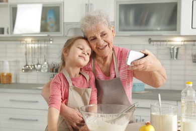 Photo of Little girl and her grandmother taking selfie in kitchen