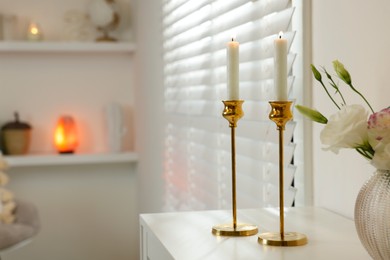 Photo of Pair of beautiful golden candlesticks on white table in room, space for text