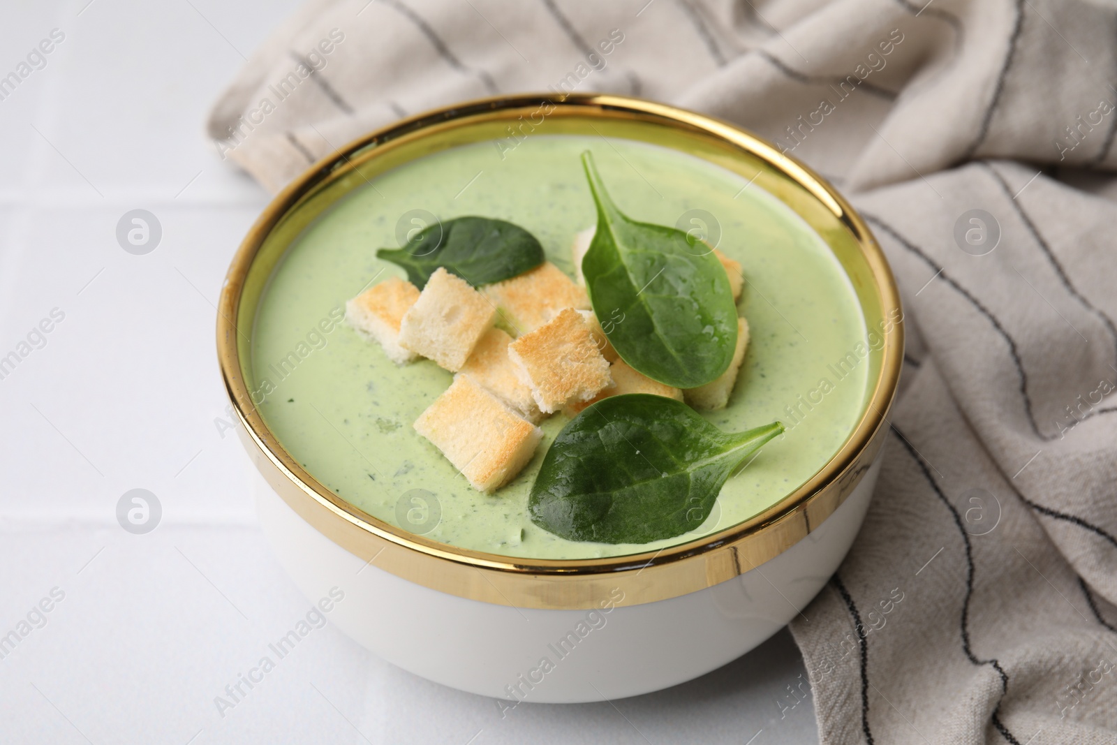 Photo of Delicious spinach cream soup with croutons in bowl on white tiled table