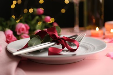 Photo of Place setting with roses and candles on pink table, closeup. Romantic dinner