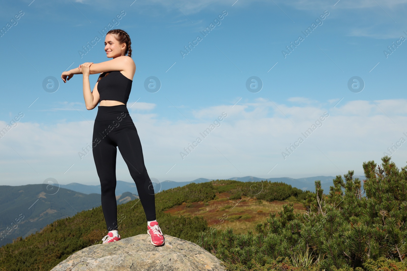 Photo of Beautiful young woman stretching on rock in mountains