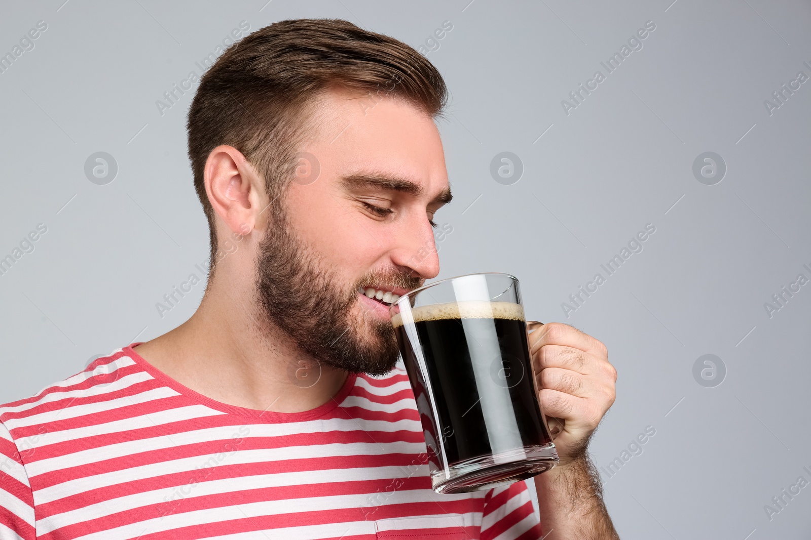 Photo of Handsome man with cold kvass on light grey background. Traditional Russian summer drink