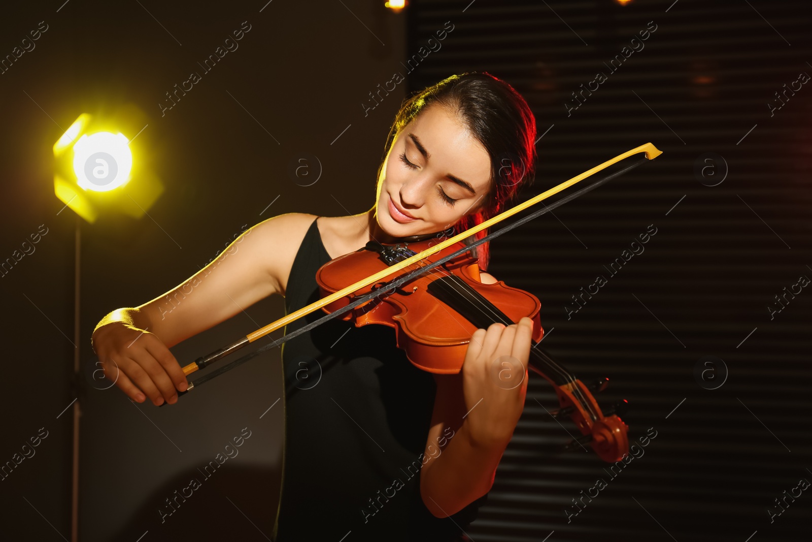 Photo of Beautiful young woman playing violin in dark room