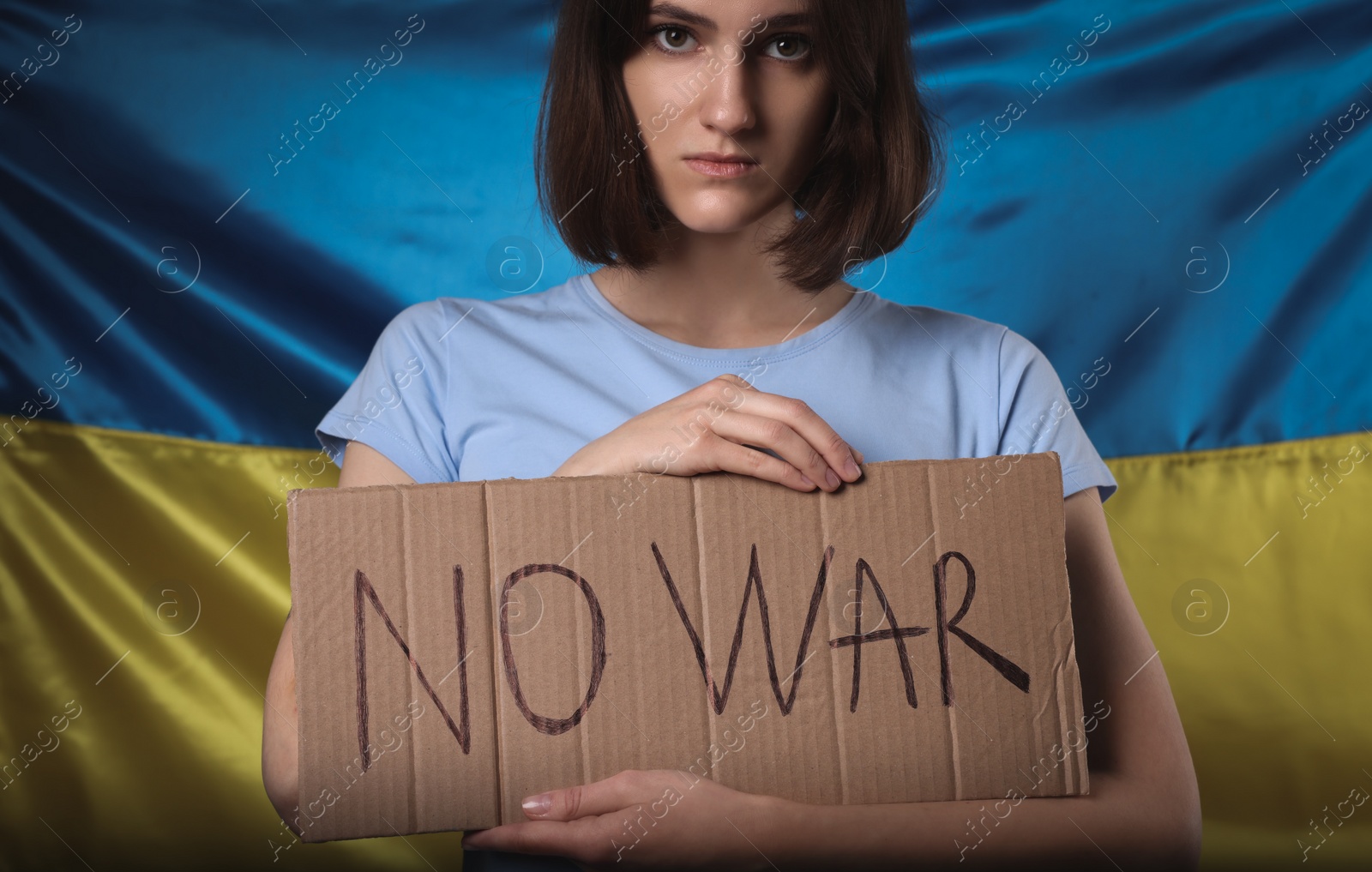 Photo of Sad woman holding poster with words No War near Ukrainian flag