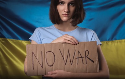 Photo of Sad woman holding poster with words No War near Ukrainian flag