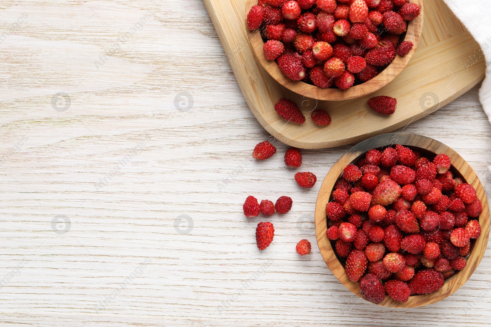 Photo of Fresh wild strawberries in bowls on white wooden table, flat lay. Space for text