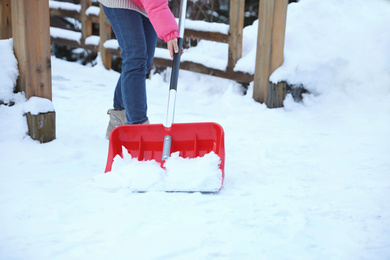 Photo of Woman cleaning snow with shovel outdoors on winter day, closeup