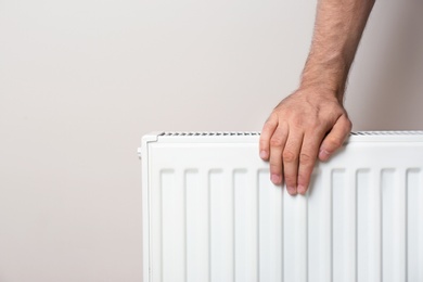 Photo of Man warming hand on heating radiator against color background. Space for text