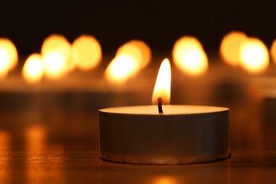 Photo of Burning tealight candle on dark surface, closeup