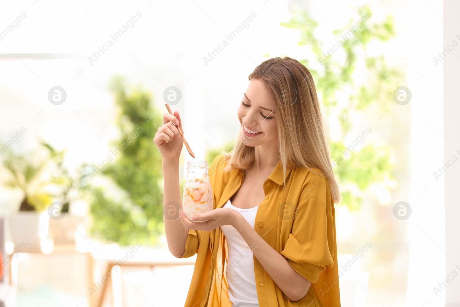 Photo of Young attractive woman eating tasty yogurt, indoors