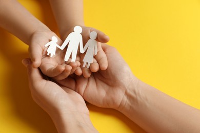 Mother and child holding paper cutout of family on yellow background, closeup