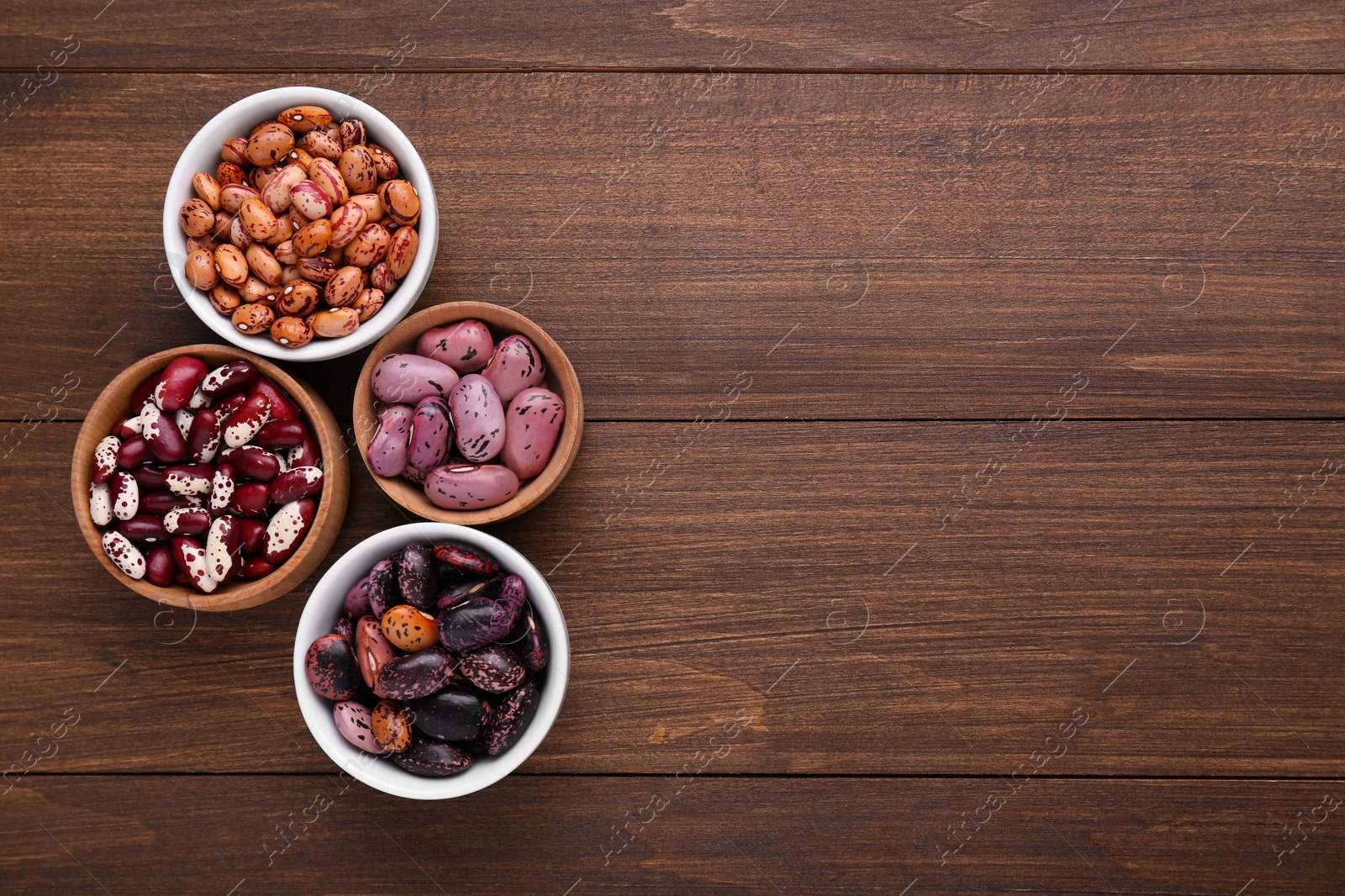 Photo of Different kinds of dry kidney beans on wooden table, flat lay. Space for text