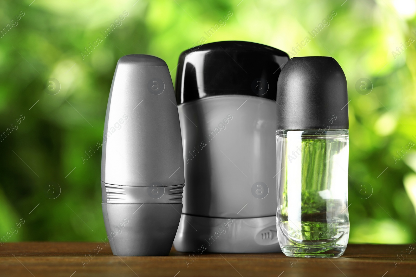 Photo of Set of different deodorants on wooden table against blurred green background