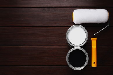 Photo of Cans of white and black paints with roller on wooden table, flat lay. Space for text