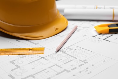 Photo of Pencil, ruler and hardhat on blueprints, closeup