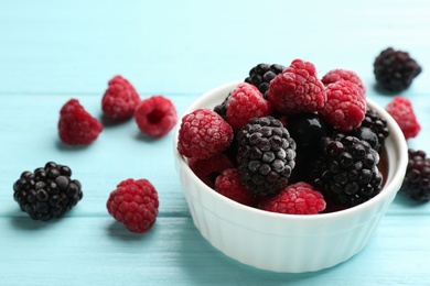 Photo of Tasty frozen blackberries and raspberries on light blue wooden table. Space for text