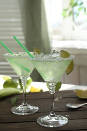 Delicious Margarita cocktail in glasses and lime on wooden table, closeup