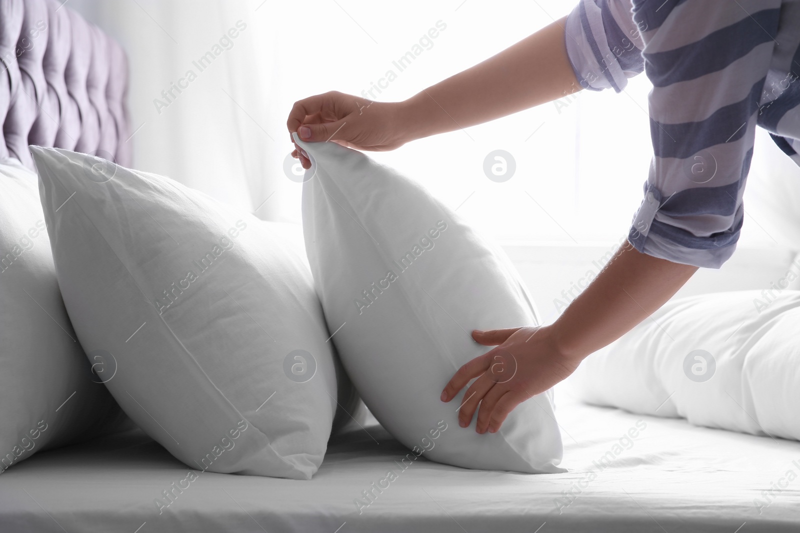 Photo of Woman fluffing white pillow on bed, closeup