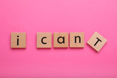 Photo of Motivation concept. Changing phrase from I Can't into I Can by removing wooden square with letter T on pink background, top view