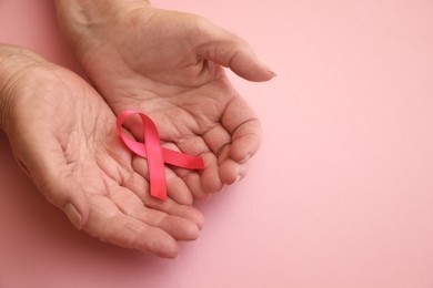 Photo of Senior woman holding pink ribbon on color background, top view with space for text. Breast cancer awareness