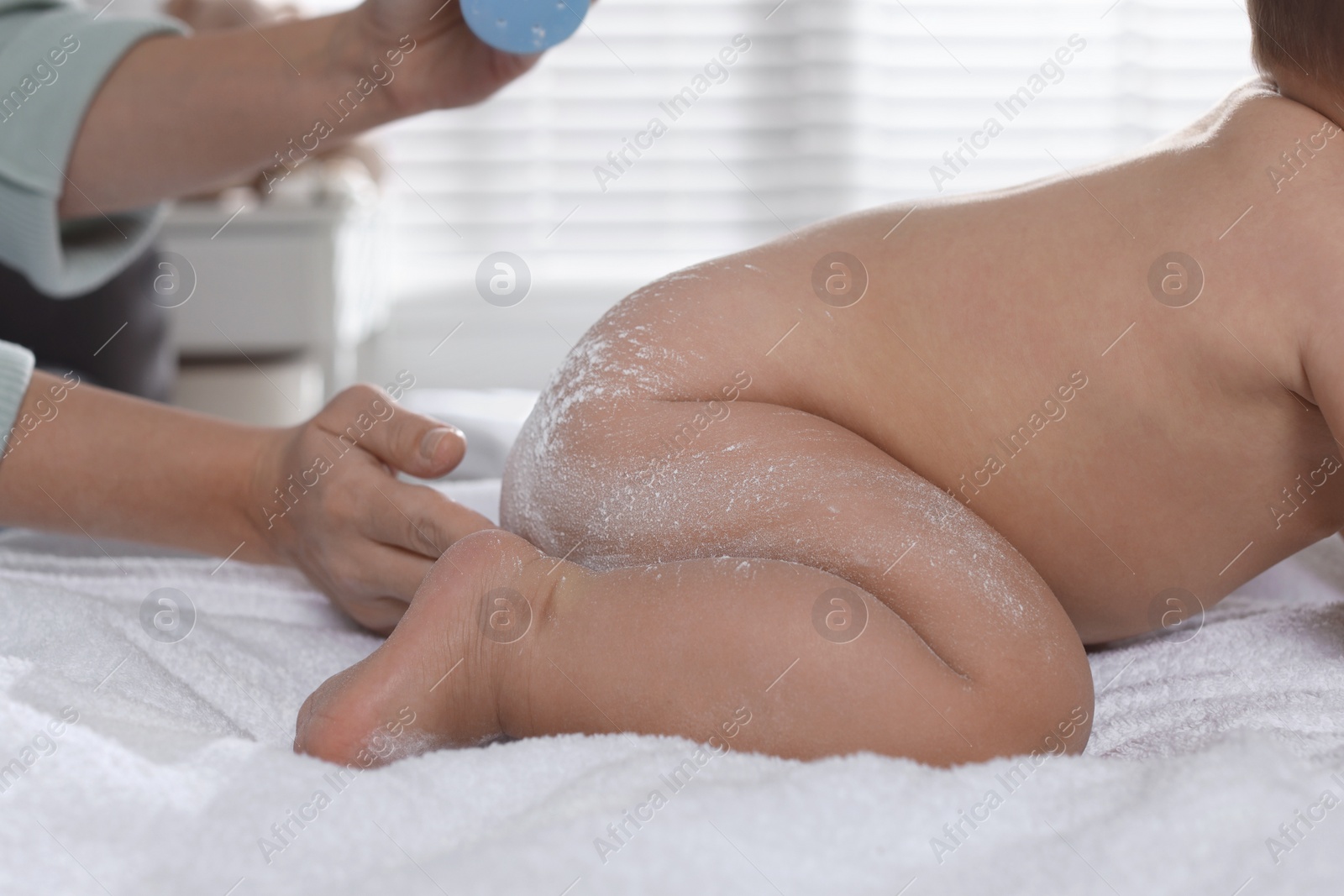 Photo of Mother applying dusting powder on her baby at home, closeup