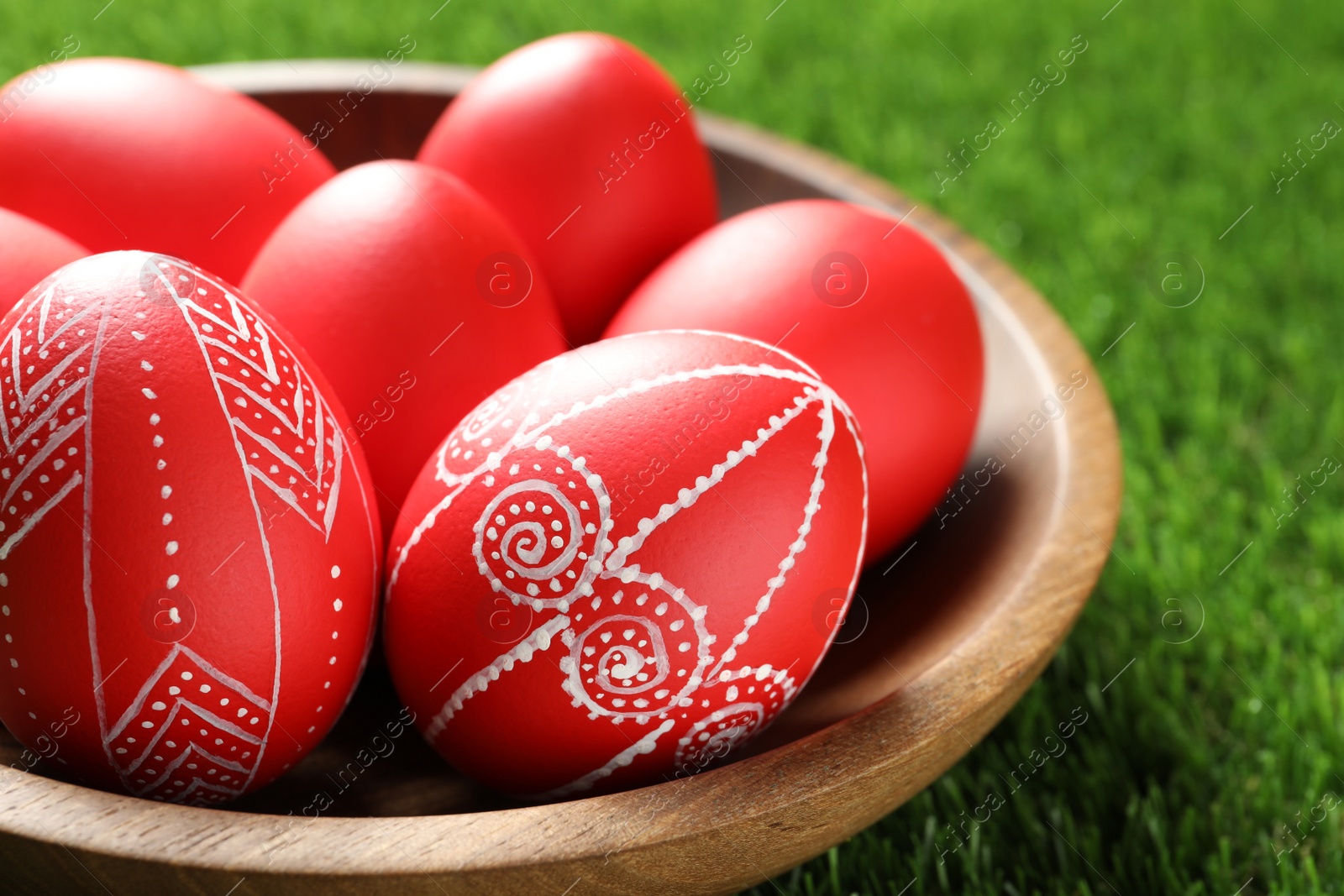 Photo of Wooden bowl with red painted Easter eggs on green grass, closeup