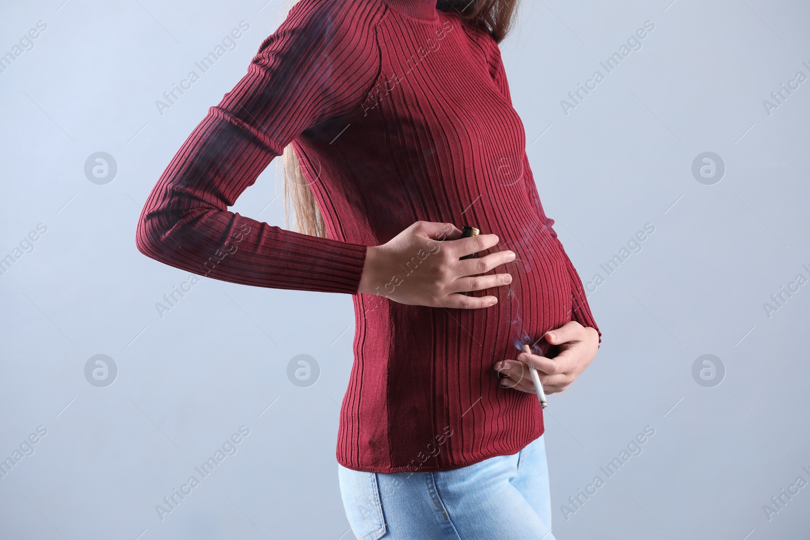 Photo of Young pregnant woman smoking cigarette on grey background, closeup. Harm to unborn baby