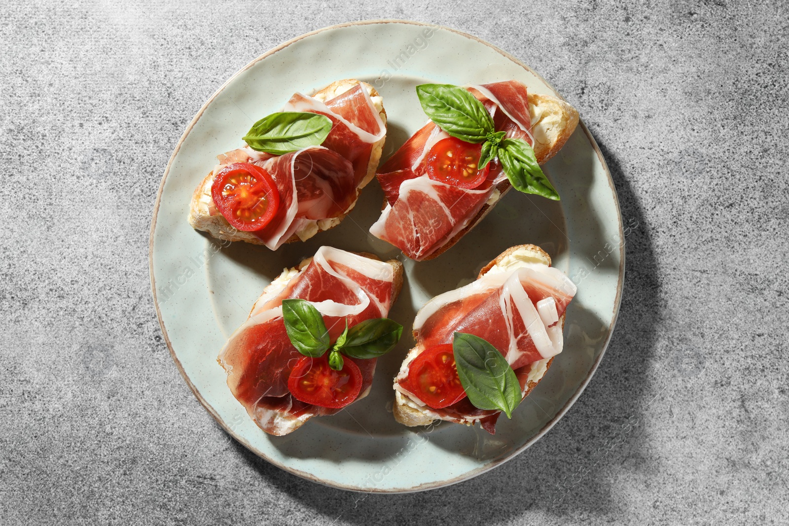 Photo of Tasty sandwiches with cured ham, basil and tomatoes on grey table, top view