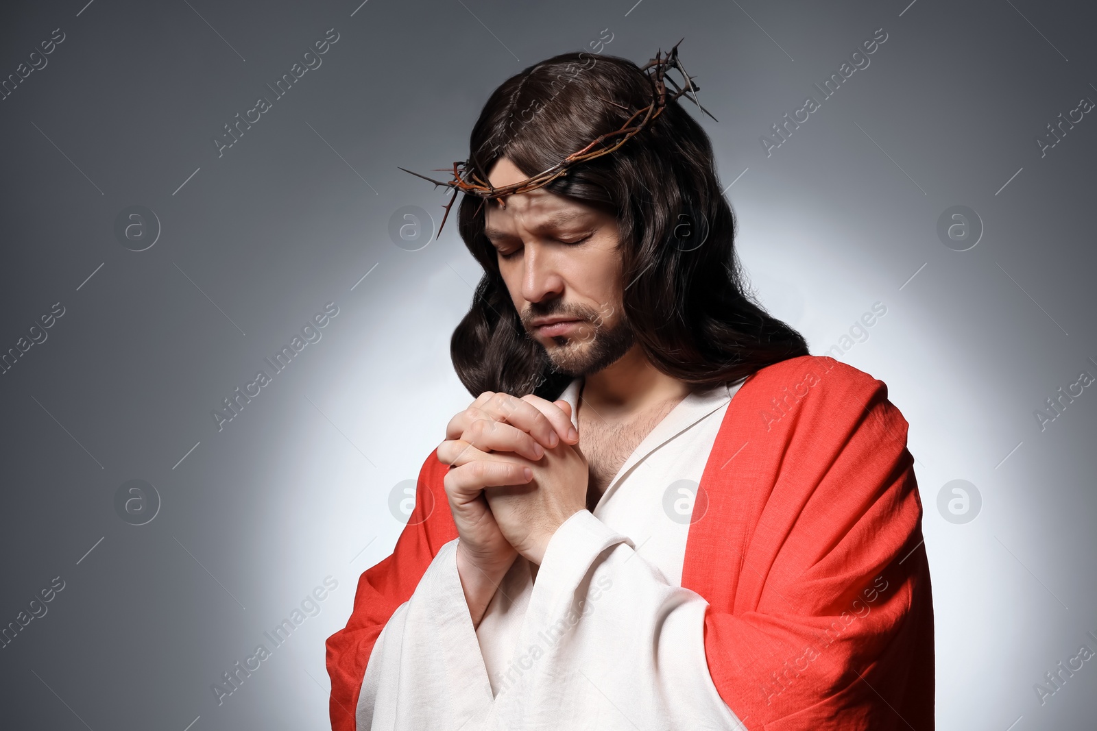 Photo of Jesus Christ with crown of thorns praying on grey background