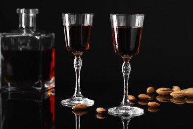 Photo of Liqueur glasses with tasty amaretto, bottle and almonds on black table, closeup