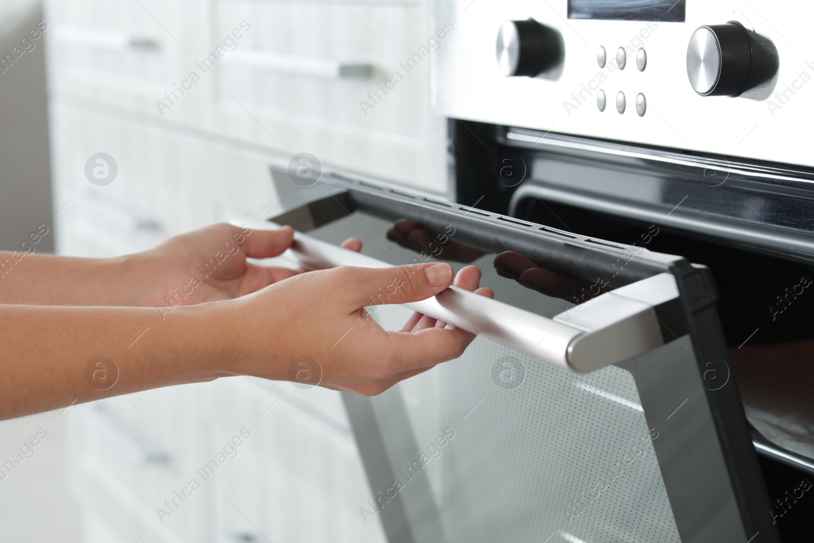 Photo of Young woman opening electric oven in kitchen, closeup