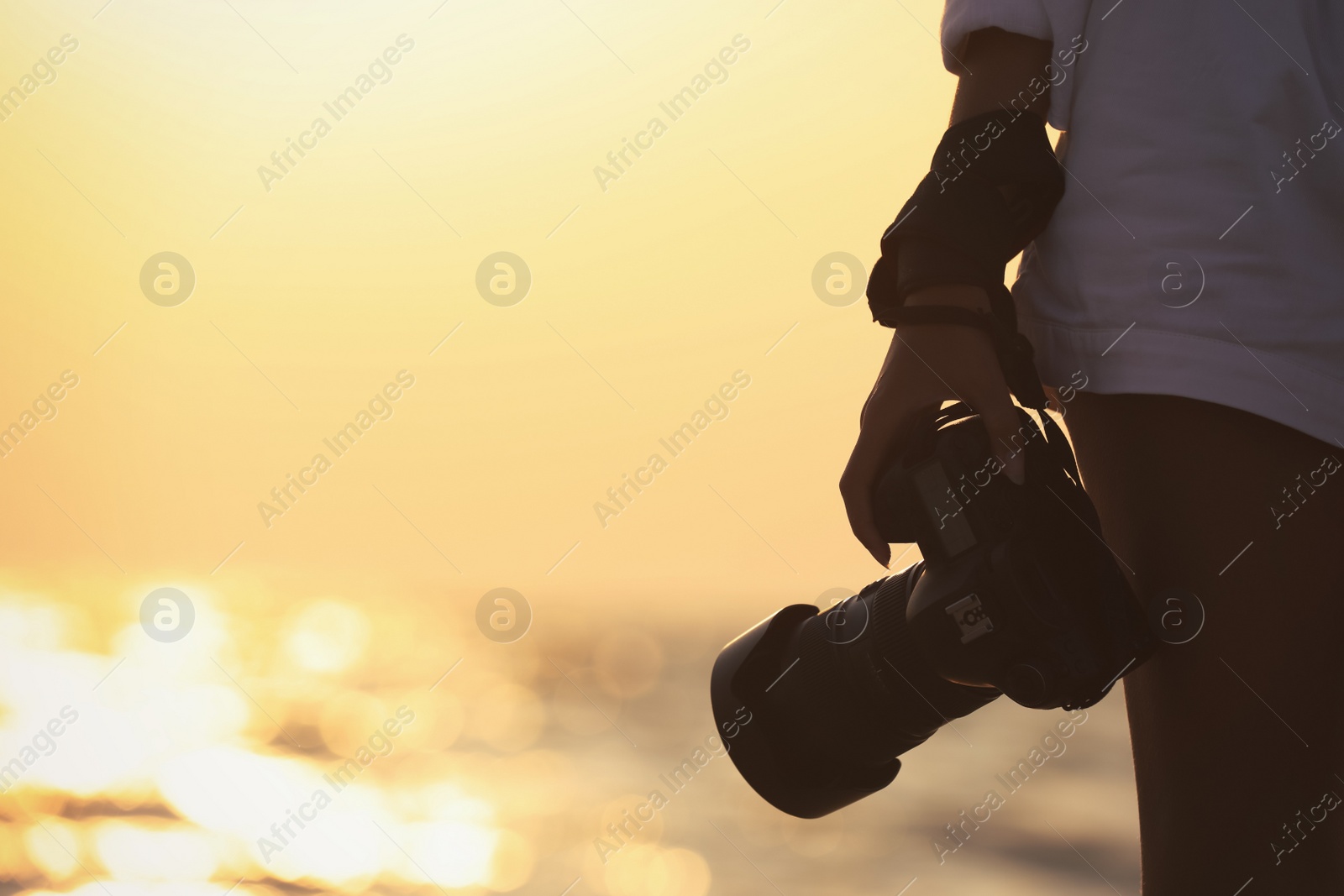 Photo of Photographer with professional camera near sea at sunset, closeup